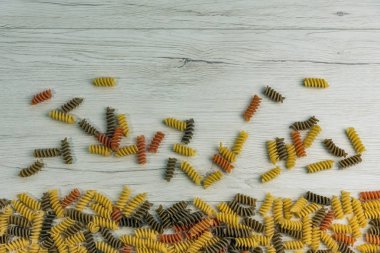 Çiğ çiğ üç renkli düdük durum buğday makarna ıspanak ve beyaz ahşap masa üzerinde domates ile.