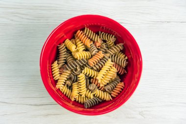 Çiğ çiğ üç renkli düdük durum buğday makarna ıspanak ve domates ile ben Beyaz ahşap masa üzerinde kırmızı bir kase.