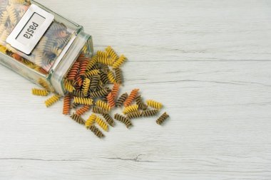 Çiğ çiğ üç renkli düdük durum buğday makarna ıspanak ve beyaz ahşap masa, üstten görünüm üzerinde bir cam kavanoza domates ile.