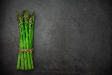 Siyah taş zemin üzerinde yeşil taze kuşkonmaz. Üst görünüm, alanı kopyala.