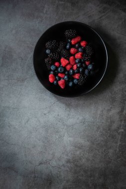 Siyah bir tabakta servis edilen organik böğürtlenler koyu metal arka planda, üst tarafta. Sağlıklı yemek kavramı. Boşluğu kopyala.
