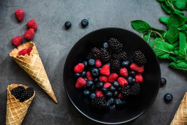Siyah bir tabakta servis edilen organik böğürtlenler koyu metal arka planda, üst tarafta. Sağlıklı gıda kavramı.