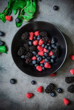 Siyah bir tabakta servis edilen organik böğürtlenler koyu metal arka planda, üst tarafta. Sağlıklı gıda kavramı.