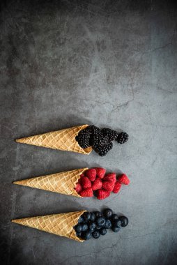 Koyu taştan arka planda waffle külahında taze böğürtlen, üst manzara. Sağlıklı yiyecekler ve çöl kavramı. Boşluğu kopyala.
