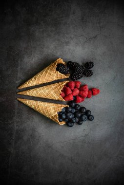 Koyu taştan arka planda waffle külahında taze böğürtlen, üst manzara. Sağlıklı yiyecekler ve çöl kavramı.