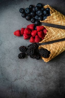 Koyu taştan arka planda waffle külahında taze böğürtlen, üst manzara. Sağlıklı yiyecekler ve çöl kavramı.