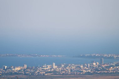 Sahil kenti Nesebar, sakin bir deniz ve açık mavi gökyüzünün altındaki uzak bir kara parçası olan orta ve yüksek binalarla ön planda uzanır..