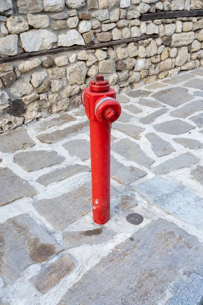 Parlak kırmızı bir yangın musluğu engebeli bir taş kaldırımda duruyor sakin bir kentin köşesinde yıpranmış bir taş duvara karşı..