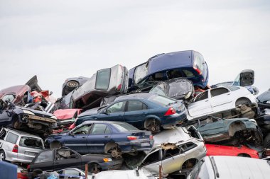 Temiz bir gökyüzünün altındaki kaotik bir hurdalıkta yığılmış arabalar otomotiv atıklarını ve geri dönüşümü sembolize ediyor..