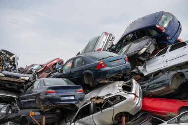 Temiz bir gökyüzünün altındaki kaotik bir hurdalıkta yığılmış arabalar otomotiv atıklarını ve geri dönüşümü sembolize ediyor..