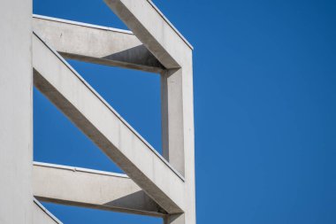 Modern beyaz beton kirişler açık mavi gökyüzüne karşı geometrik şekiller oluşturuyor.