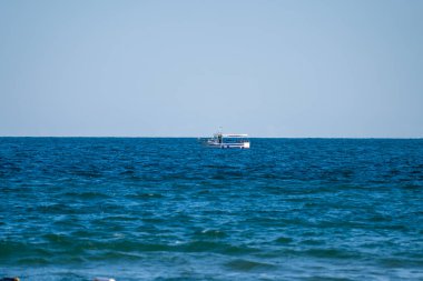 Sakin dalgalarla çevrili bulutsuz bir gökyüzünün altında, derin mavi denizde huzur içinde yüzen yalnız bir tekne..