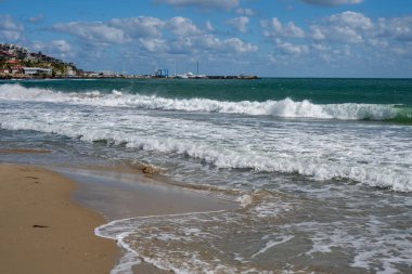 Yumuşak dalgalar, yumuşak bulutlar ve açık bir ufuk ile huzurlu sahil sahnesi.