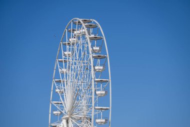 Eşit aralıklı kamaraları olan yüksek beyaz bir dönme dolap açık mavi gökyüzüne doğru yükseliyor..