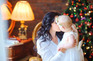 güzel anne öper ve neşeli Noel ağacı yakın bir sandalyede otururken sarılarak