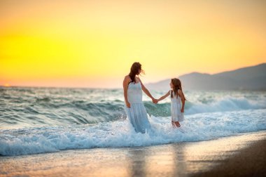 Anne kızıyla birlikte gün batımında sahilde yürüyor, el ele tutuşup dalgalar üzerinde yürümek