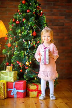 Noel ağacı yakınındaki elinde bir hediye ile mutlu küçük kız