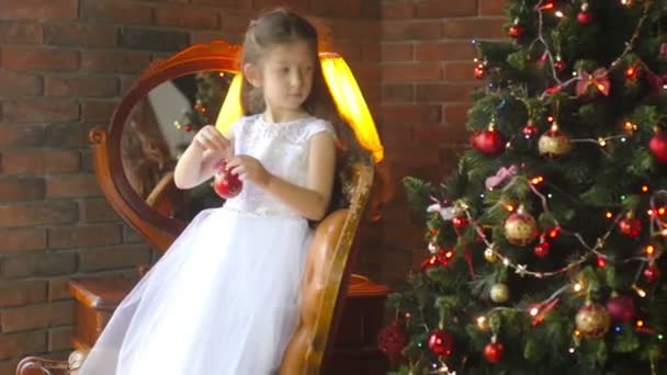 ドレスを着た美しい少女は 家の中のクリスマス ツリーを飾る 待っている休日 — ストック動画
