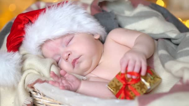 クリスマス 帽子はささやかな贈り物を保持しているバスケットに横たわって眠っているサンタ クロースの生まれたばかりの赤ちゃん — ストック動画