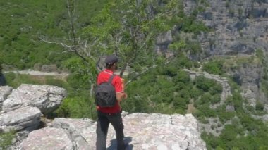 Sırt çantası olan bir gezgin vadinin kenarına doğru yürür ve sevinçle ellerini Wanderlust yükseltir