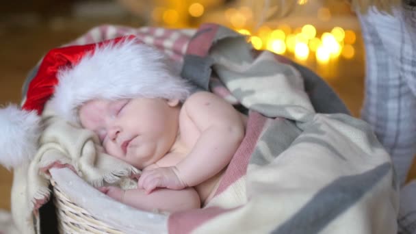 クリスマス 帽子は明るい休日背景にバスケットに横たわって眠っているサンタ クロースの生まれたばかりの赤ちゃん — ストック動画