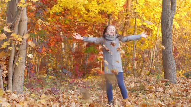 fröhliches Mädchen, das im Herbstpark spielt und Spaß hat, Blätter wirft und lacht