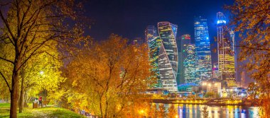 Moskova Nehri setin bir parkın Moskova'dan bir iş merkezinin gökdelenler Panoraması, gece ışıkları suda yansıtılır, insanlar akşam parkta yürüyüş