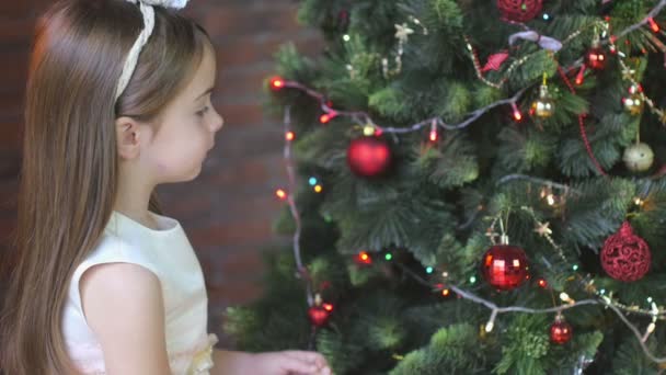 美丽的小女孩在节日礼服装饰圣诞树与球 — 图库视频影像