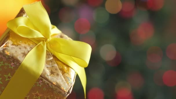 特写女孩打开一个礼物在金色的纸与黄色丝带 在明亮的节日背景 — 图库视频影像