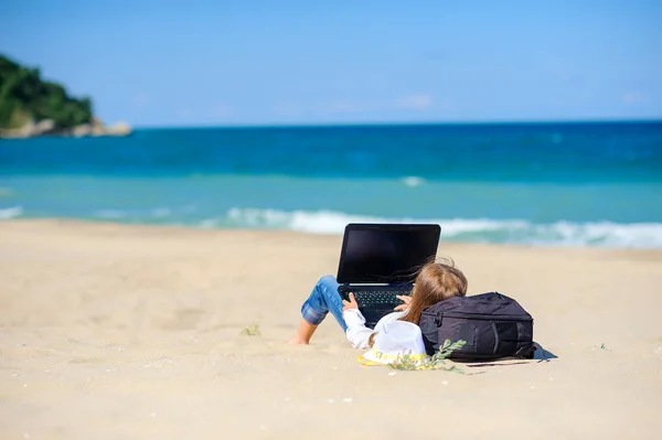 work in travel, a teen girl lies on the beach with a laptop. freelance