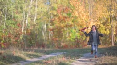 Şirin Küçük Kız Autumn Park 'ta Uçak Modeli Çalıştırıyor ve Çalıştırıyor. Çocuklar oyuncak uçakla oynarlar. Yavaş bir hareket yap. Mutlu çocukluk kavramı.
