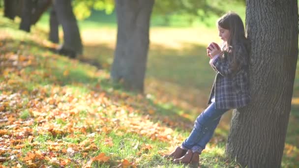 Маленька Дівчинка Пальті Стоїть Леонінг Дереві Парку Сонячної Осені Їсть — стокове відео
