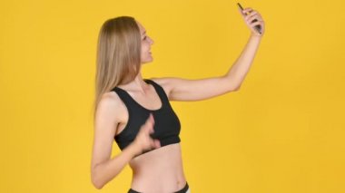 Gülümseyen fit kız sarı arka planda izole edilmiş spor egzersizinden sonra selfie çekiyor. Akıllı telefon eğitimi almış bir oto portre.