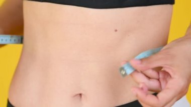 Yakın plan Genç Sıska Kız Ölçü Bantla Belini Ölçüyor. Sarı arka planda izole edilmiş. fitness kavramları.