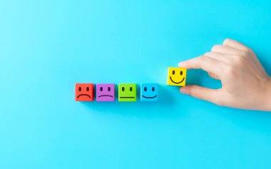 Müşteri memnuniyeti geri bildirim konsepti. Müşteri memnuniyetini, olumlu geri bildirimi, derecelendirme ölçeğini, duygusal deneyimi temsil eden renkli duygu simgelerinden el ile gülen yüz bloğu seçmek,