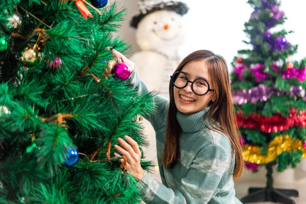Mutlu Asyalı kadın portresi eğlenceli aktiviteler yapıyor Noel ağacını süslerken evde Noel arifesi, şenlik ve etkinlik kutlaması yapıyor.