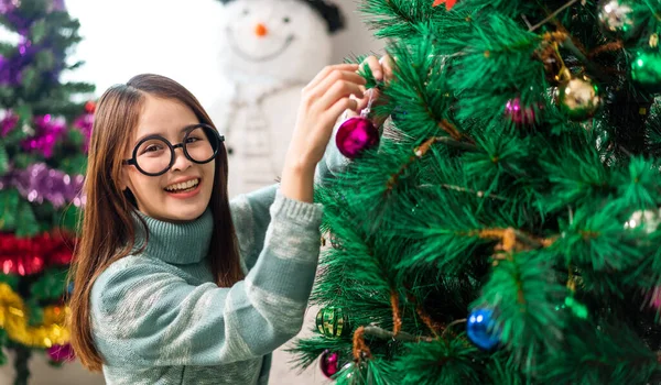 Mutlu Asyalı kadın portresi eğlenceli aktiviteler yapıyor Noel ağacını süslerken evde Noel arifesi, şenlik ve etkinlik kutlaması yapıyor.