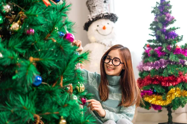 Mutlu Asyalı kadın portresi eğlenceli aktiviteler yapıyor Noel ağacını süslerken evde Noel arifesi, şenlik ve etkinlik kutlaması yapıyor.