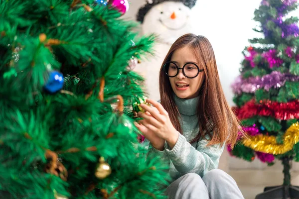 Mutlu Asyalı kadın portresi eğlenceli aktiviteler yapıyor Noel ağacını süslerken evde Noel arifesi, şenlik ve etkinlik kutlaması yapıyor.