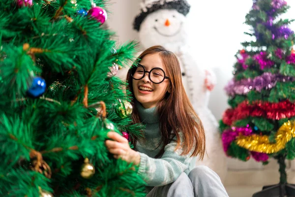 Mutlu Asyalı kadın portresi eğlenceli aktiviteler yapıyor Noel ağacını süslerken evde Noel arifesi, şenlik ve etkinlik kutlaması yapıyor.