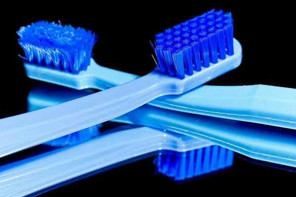 New and used blue professional soft toothbrushes with lot of bristles in straight cut on black mirror background.