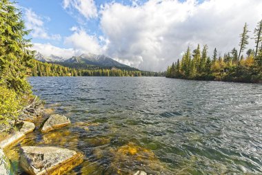 Yüksek Tatras dağlar Peaks'e Strbske Plesolake waterfront bulutlar. Orman, karla kaplı kayalık tepeler ve ikonik dağ otel Güneş yaktı.