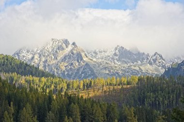 Yüksek Tatras dağlar Peaks'e Strbske Plesolake waterfront bulutlar. Güneş ormanı yaktı ve kayalık doruklarına kar kaplı.