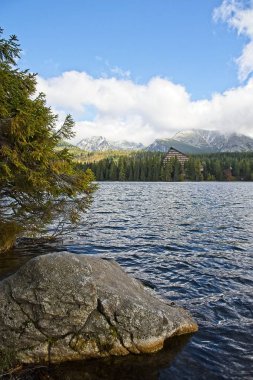 Yüksek Tatras dağlar Peaks'e Strbske Plesolake waterfront bulutlar. Orman, karla kaplı kayalık tepeler ve ikonik dağ otel Güneş yaktı.
