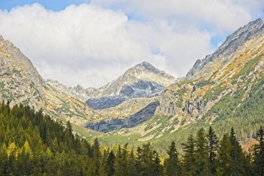 Yüksek Tatras dağlar Peaks'e Strbske Plesolake waterfront bulutlar. Güneş ormanı yaktı ve kayalık doruklarına kar kaplı.