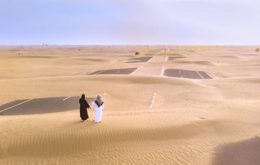emirati couple on a sand covered road ina desert near Dubai clipart