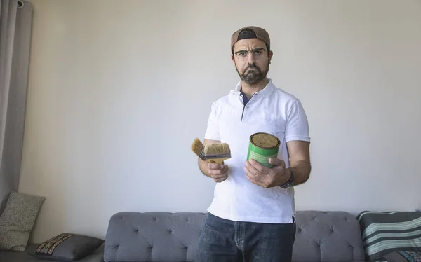 arab man holding tin of paint and brushes and looking confused