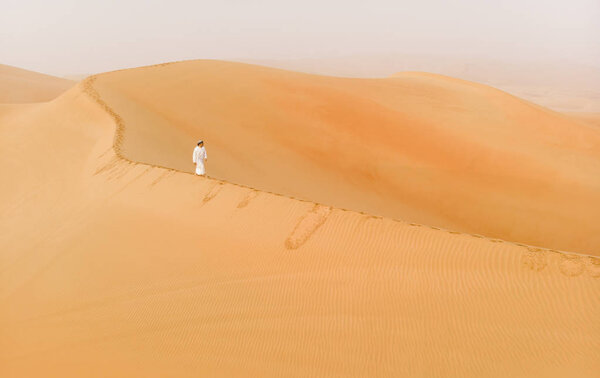 Madinat Zayed, United Arab Emirates - 22nd December, 2018: man in traditional emirati outfit walking in massive sand dunes of Liwa desert