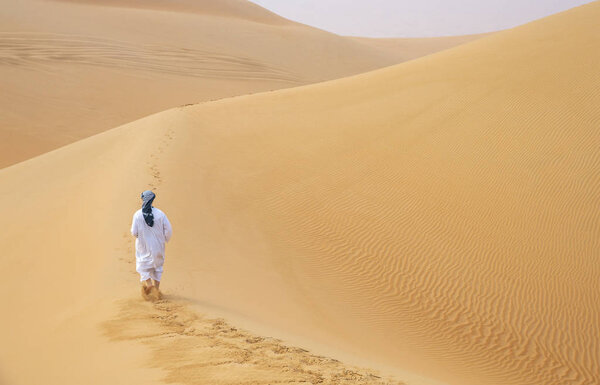 man in traditional emirati outfit walking in massive sand dunes of Liwa desert