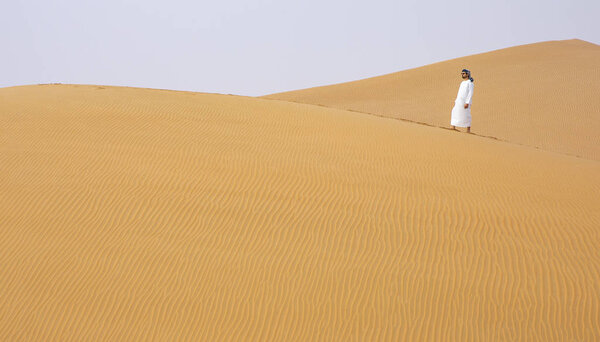 man in traditional emirati outfit walking in massive sand dunes of Liwa desert